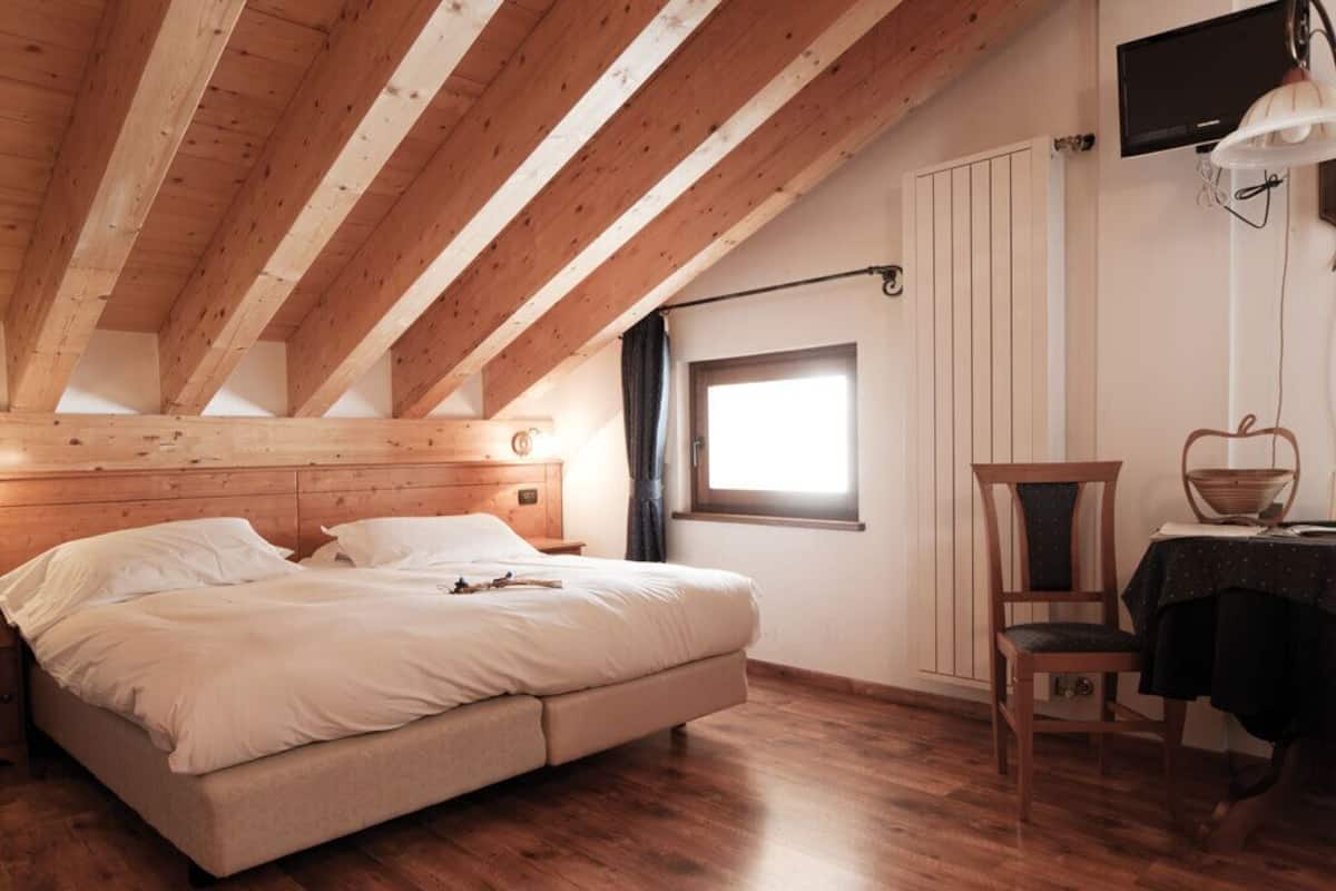 A bedroom with a wooden ceiling, a bed, a nightstand, a chair, a table, and a window.