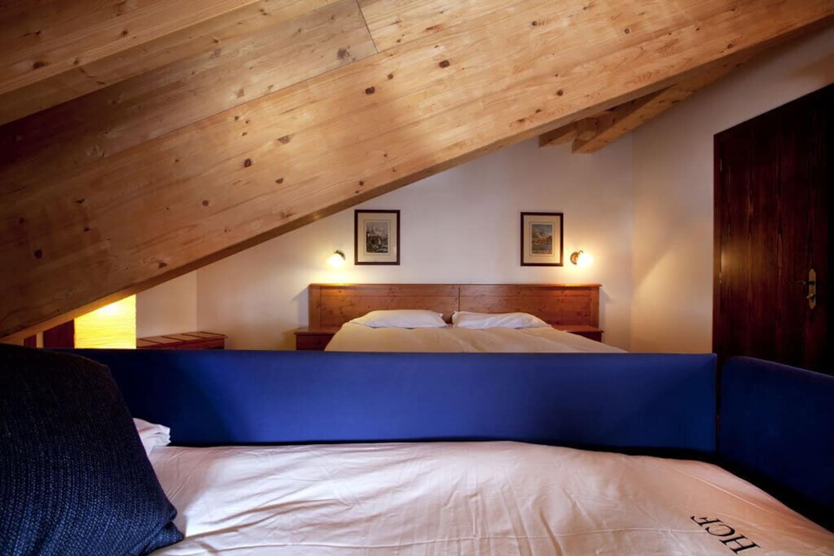 A bedroom with a sloped ceiling, a wooden headboard, a bed with white bedding, and two wall-mounted lights.