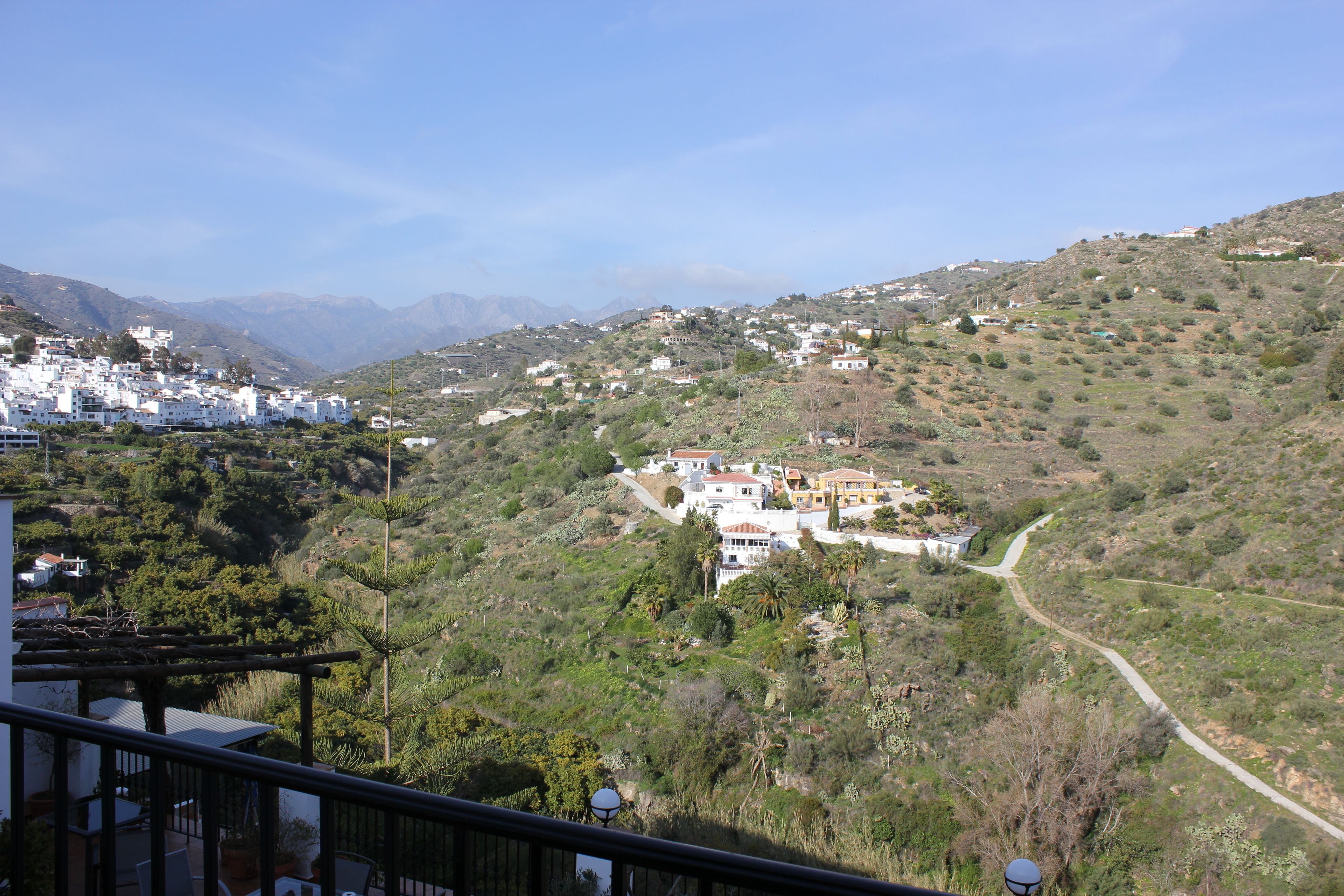 Une ville perchée sur une colline, avec des bâtiments blancs, une route sinueuse et une végétation luxuriante.