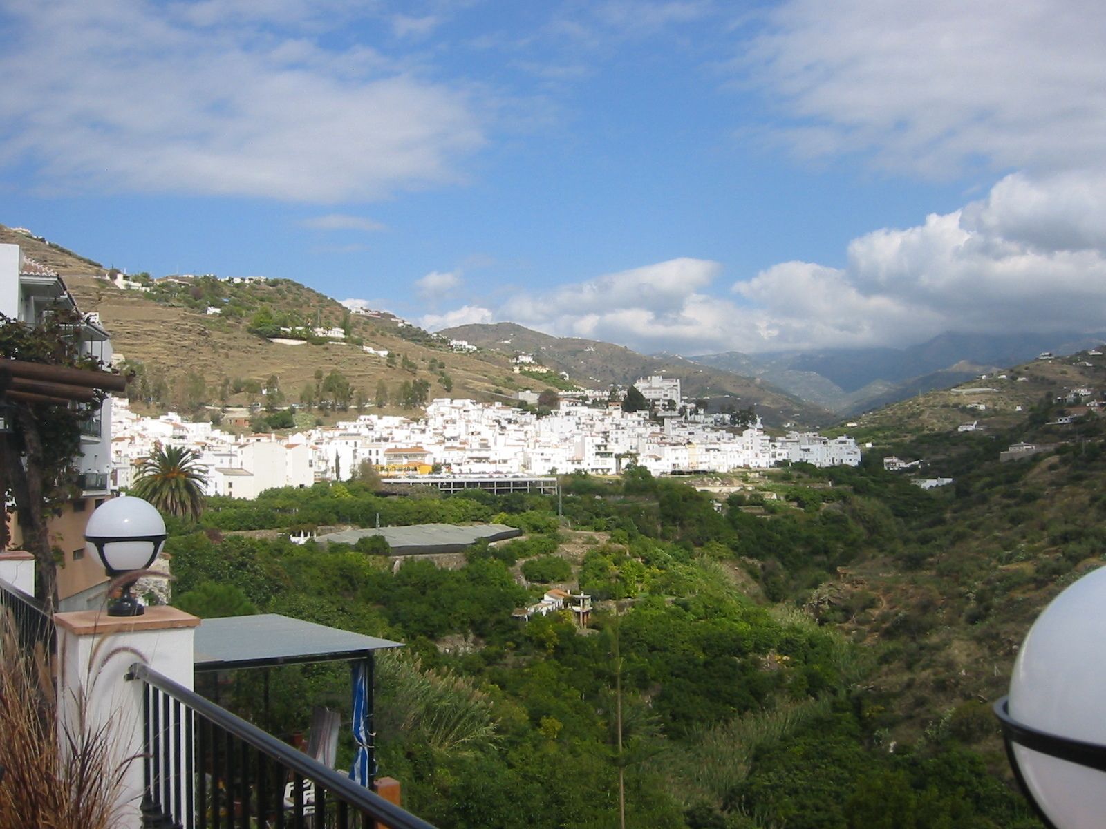 Une ville perchée sur une colline, avec des bâtiments blancs, une végétation luxuriante et un ciel dégagé.