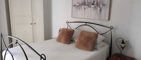A bedroom with a bed, a nightstand, a painting, and a wardrobe.