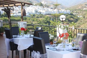 Mesa preparada para una comida con vista a un pueblo y colinas al fondo.