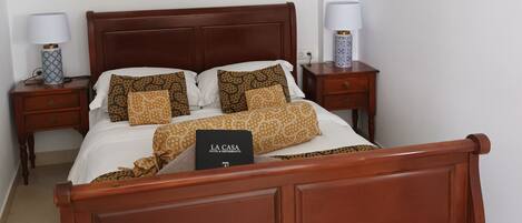 Una cama bien hecha con almohadas estampadas, un cabecero de madera y un cartel que indica que pertenece a La Casa Hotel & Restaurant.