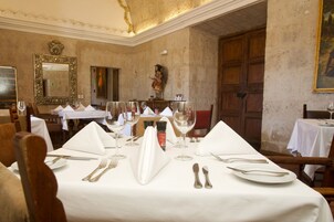 Un comedor con mesas dispuestas para una comida, incluyendo copas de vino, cubiertos y servilletas.