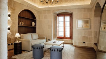 Un salon comprenant un canapé, des poufs, une table basse, une lampe, un lustre, une bibliothèque et une fenêtre.
