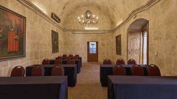 Un salón de conferencias con mesas y sillas, una araña de cristal y cuadros en las paredes.