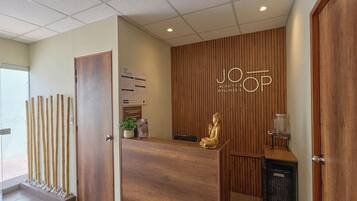 Un área de recepción con un mostrador de madera, una estatua de Buda, un letrero de JOOP Beauty & Wellness y una mampara de bambú vertical.