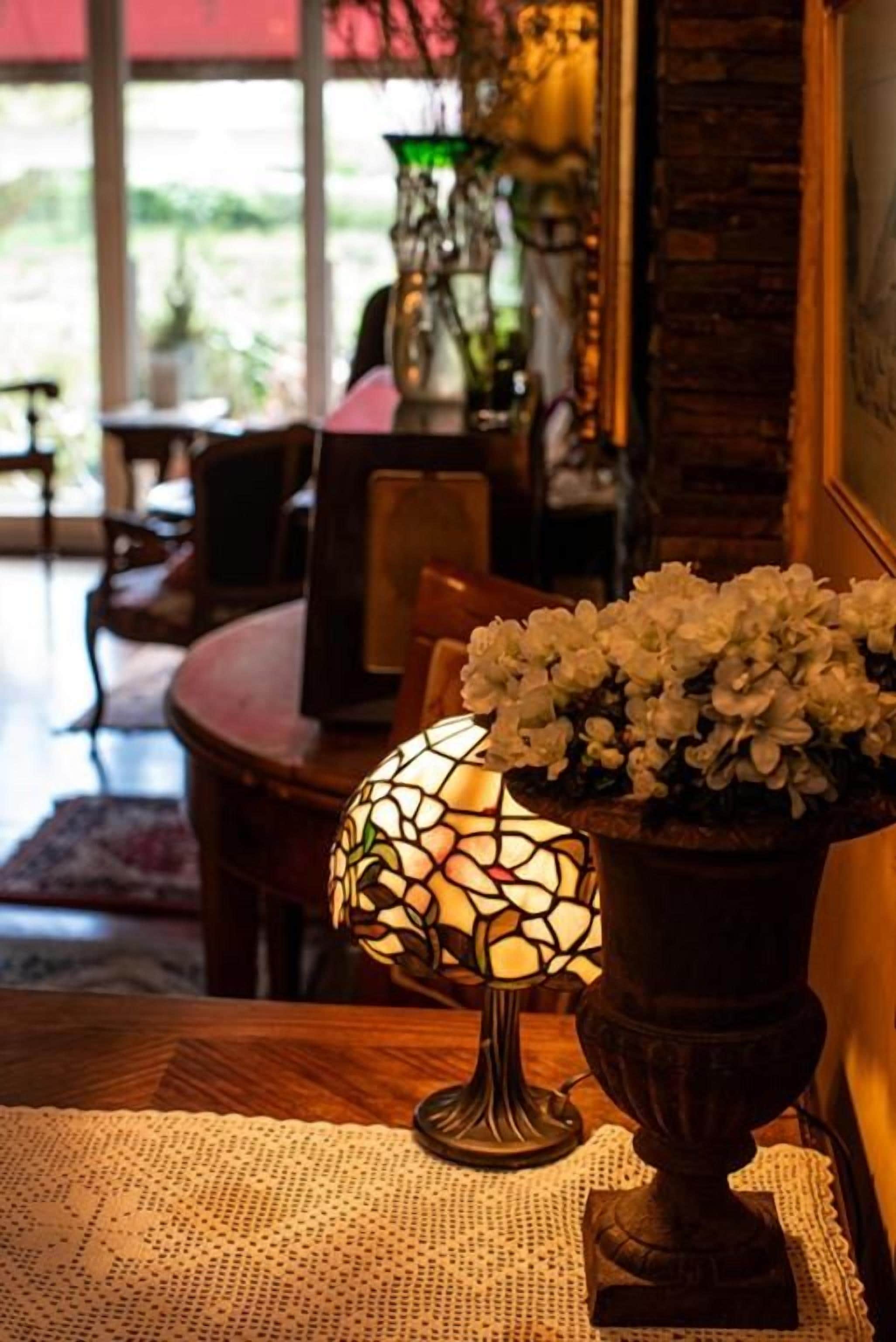 Una mesa con una lámpara de mosaico y un jarrón con flores blancas.