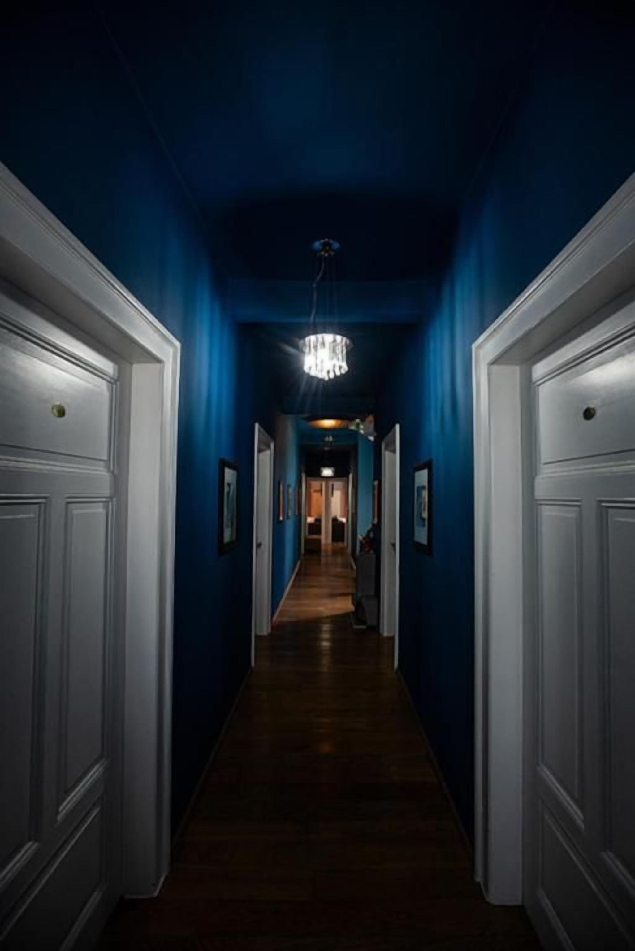 Un couloir orné d’un lustre, avec des portes blanches et des tableaux encadrés accrochés aux murs.