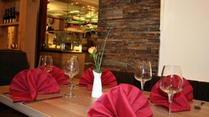 A restaurant setting with a wooden table set for two, red napkins, and wine glasses. - Hotel Rosengarten Kehl (Kehl)