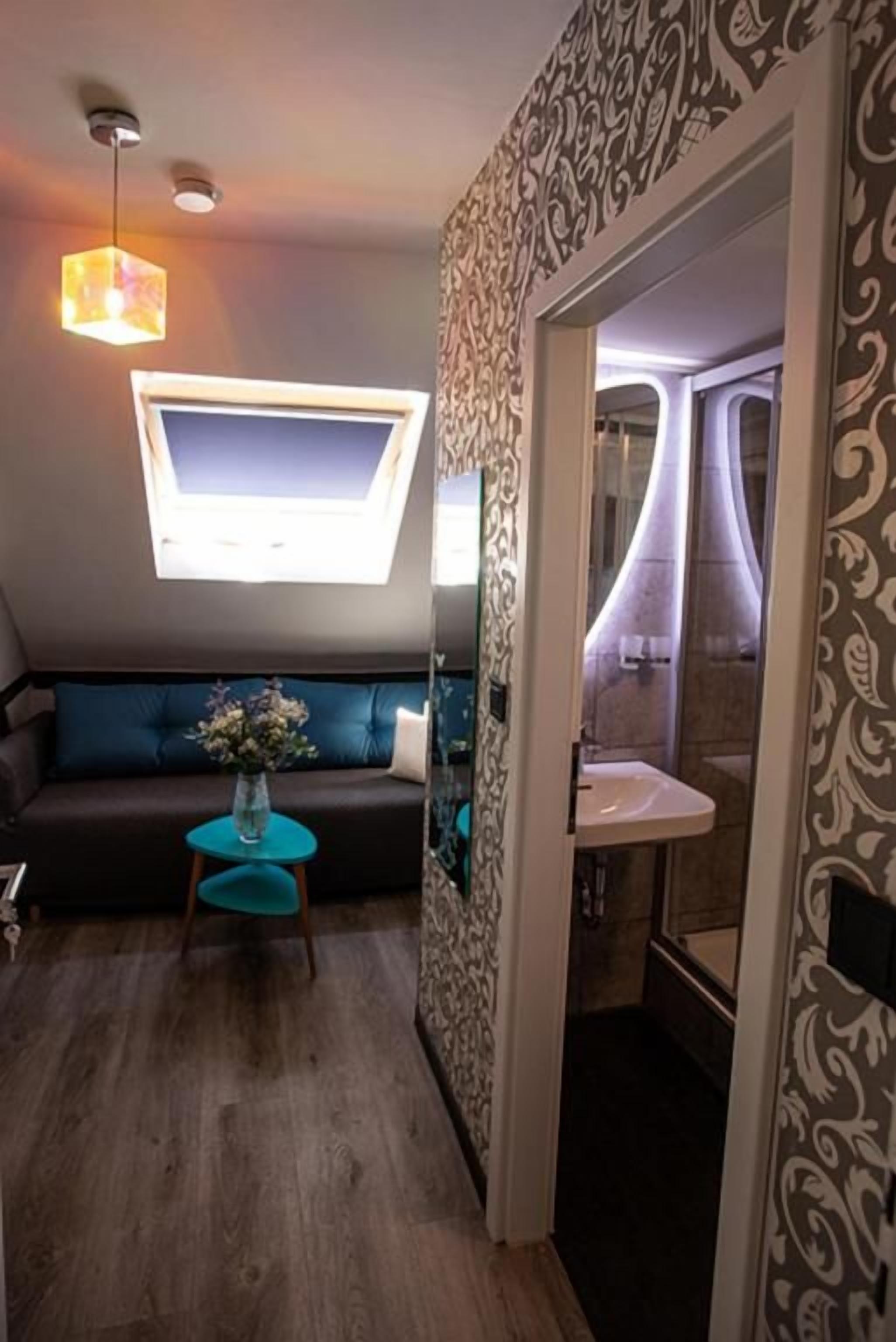 Un espacio habitable pequeño con un sofá, una mesita redonda, un televisor montado en la pared y un baño visible a través de una puerta abierta.