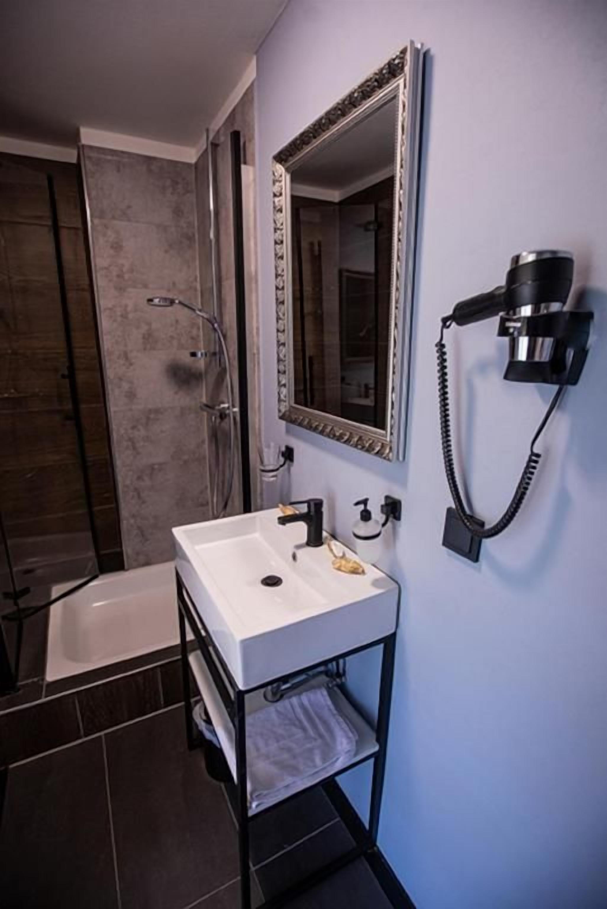 Un baño con lavamanos blanco, un espejo y un secador de pelo montado en la pared.