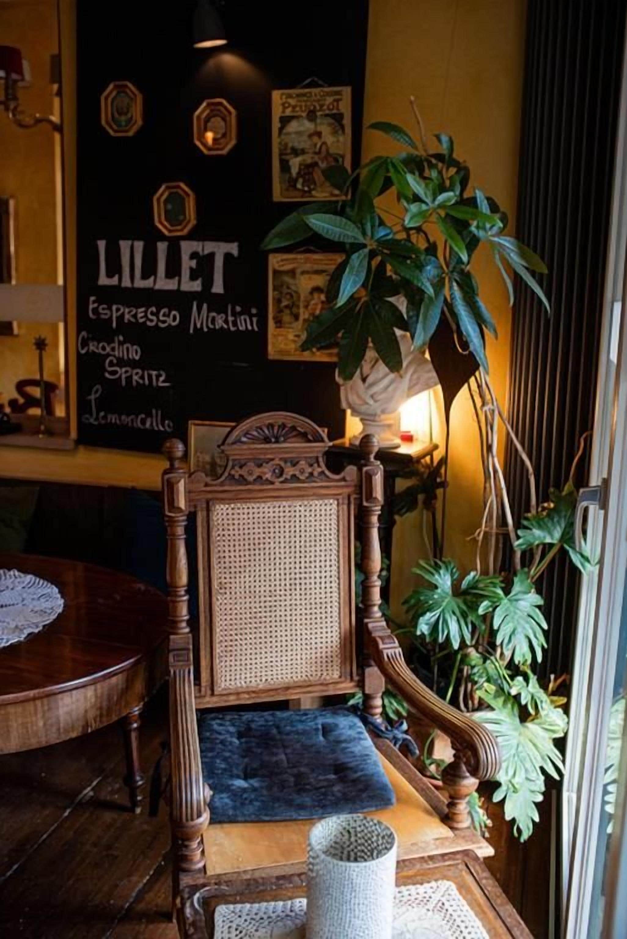 A wooden chair with a woven backrest, a small round table with a lace doily, and a potted plant.
