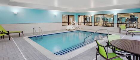 Una piscina interior con suelo de baldosas, una escalera de piscina y algunas sillas de descanso.