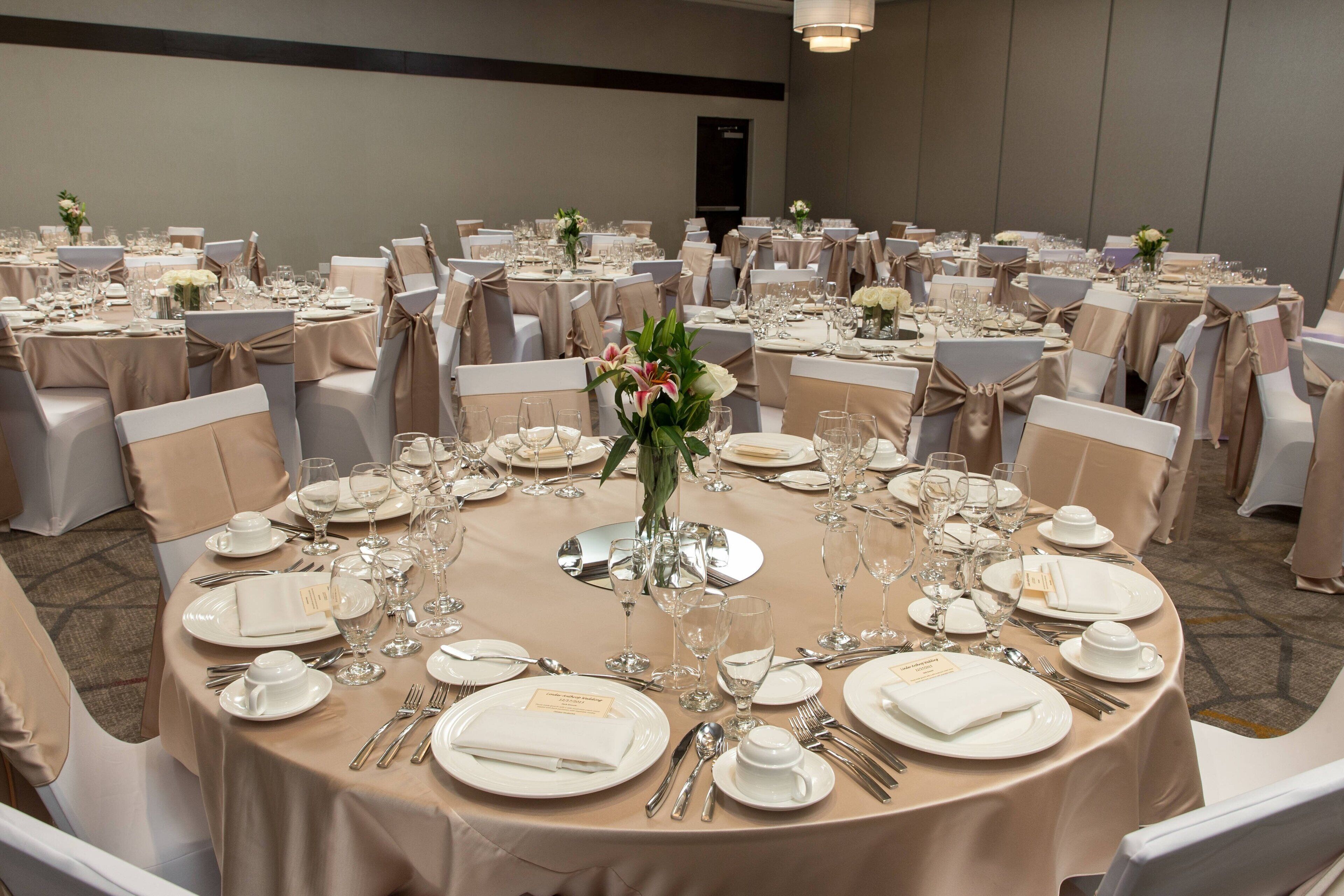 A banquet hall with round tables set for a formal event, complete with white tablecloths, silverware, and floral centerpieces.
