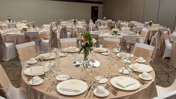 A banquet hall with round tables set for a formal event, complete with white tablecloths, silverware, and floral centerpieces.