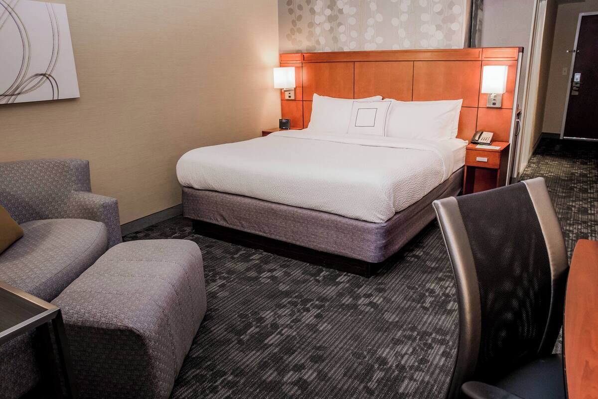 Habitación de hotel con una cama grande, dos sillones, un escritorio y una mesita de noche con lámpara y teléfono.
