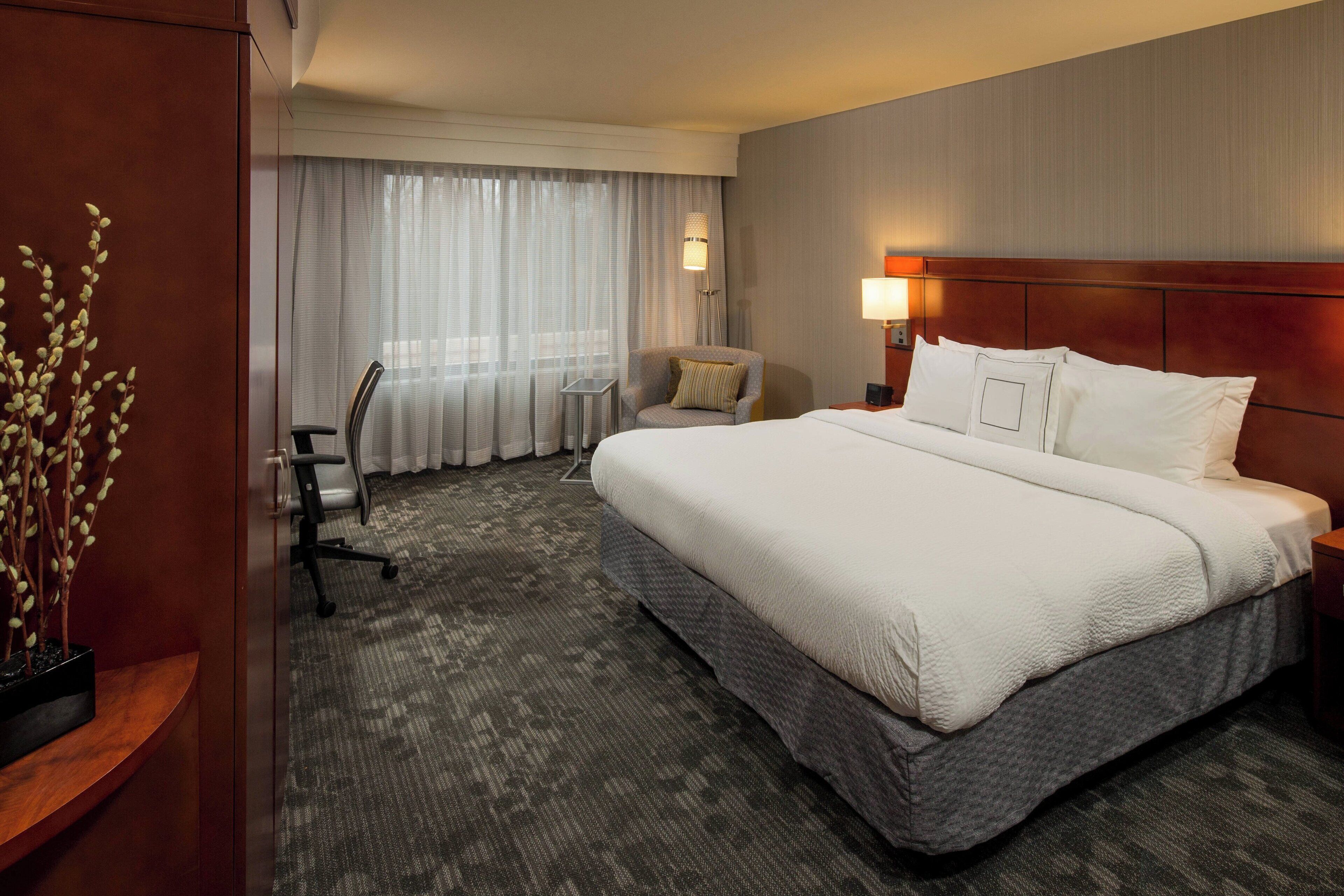 Quarto de hotel com uma cama grande, uma escrivaninha, uma cadeira e uma mesinha.