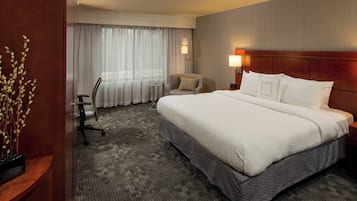 Quarto de hotel com uma cama grande, uma escrivaninha, uma cadeira e uma mesinha.