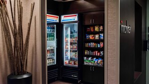 A corner of a room with two refrigerators stocked with snacks and drinks, a decorative vase with branches, and a wall with a 'market' sign. - Courtyard Marriott Lafayette (Lafayette)