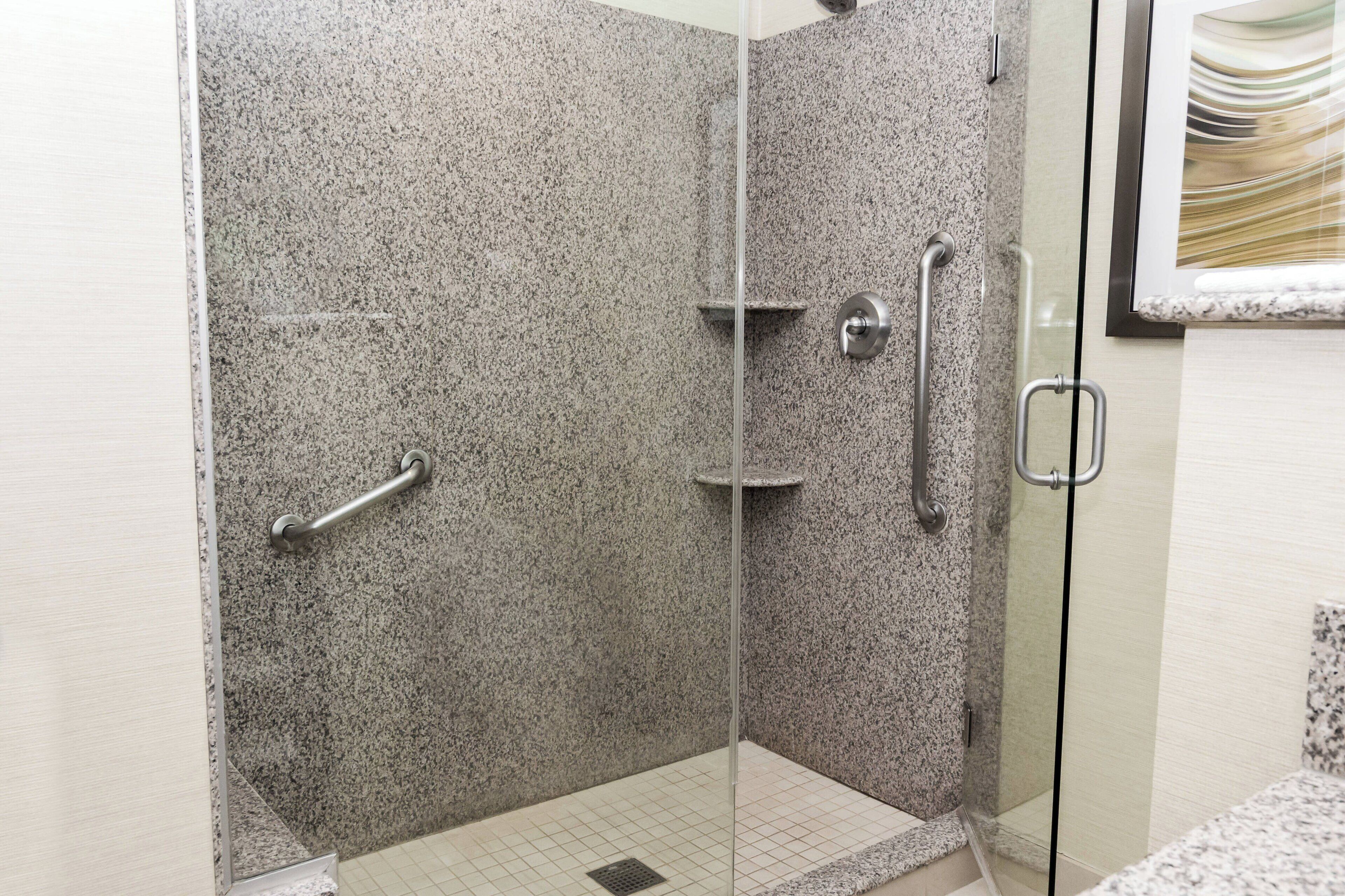 A shower with a glass door, granite walls, and a metal grab bar.