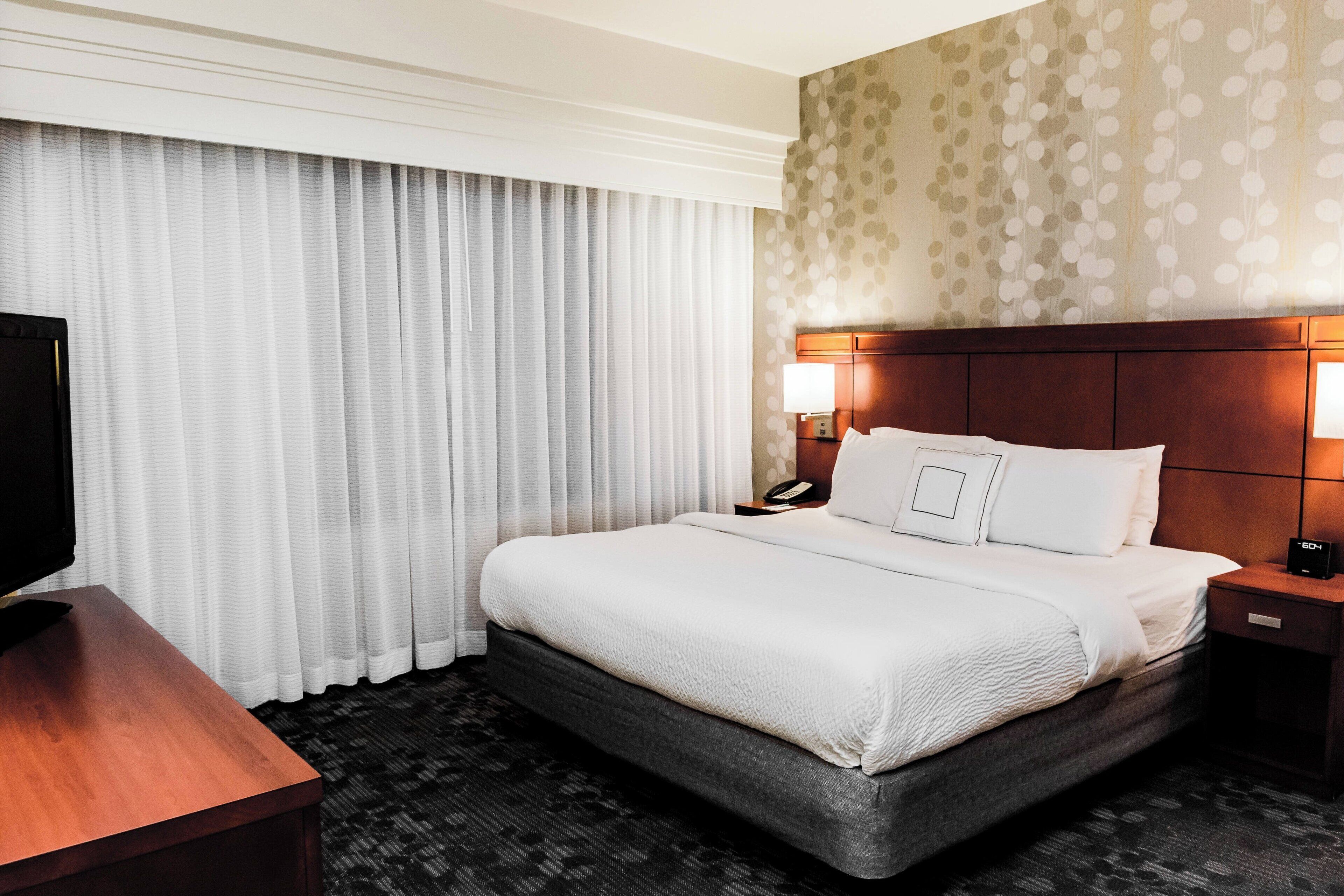Ein Hotelzimmer mit einem großen Bett, einem Nachttisch aus Holz, einem Fernseher und einer Wand mit Muster.