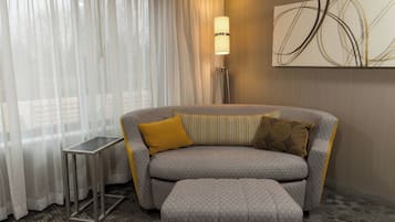 A modern hotel room with a grey sofa, a small side table, and a floor lamp.