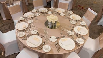 A round table set for a formal event with white chairs, a beige tablecloth, and a central floral arrangement.