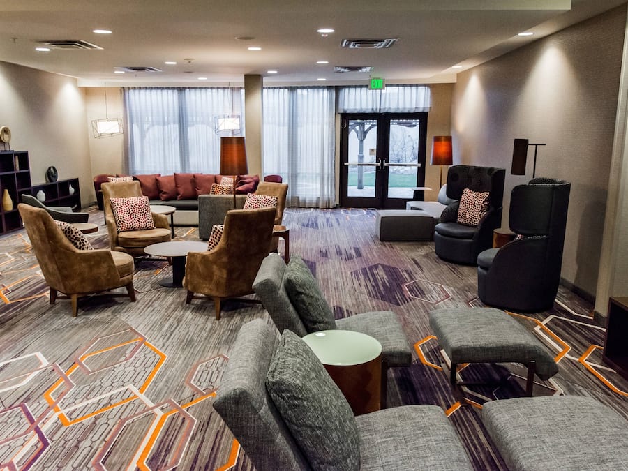 A hotel lobby with sofas, armchairs, a coffee table, and a bookshelf.