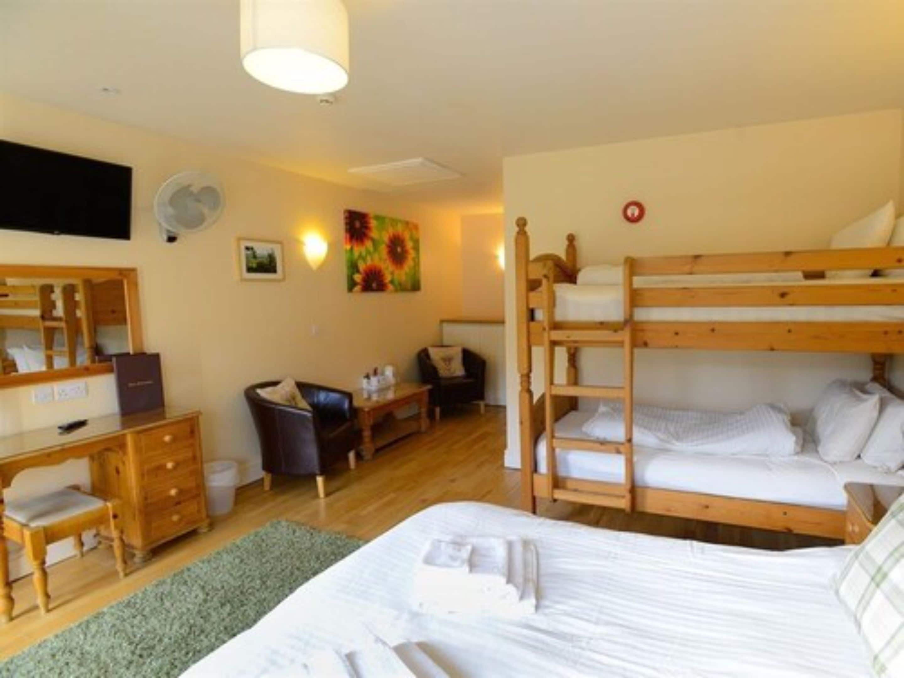 A compact hotel room with a bunk bed, a desk with a chair, a dresser, and a small table.