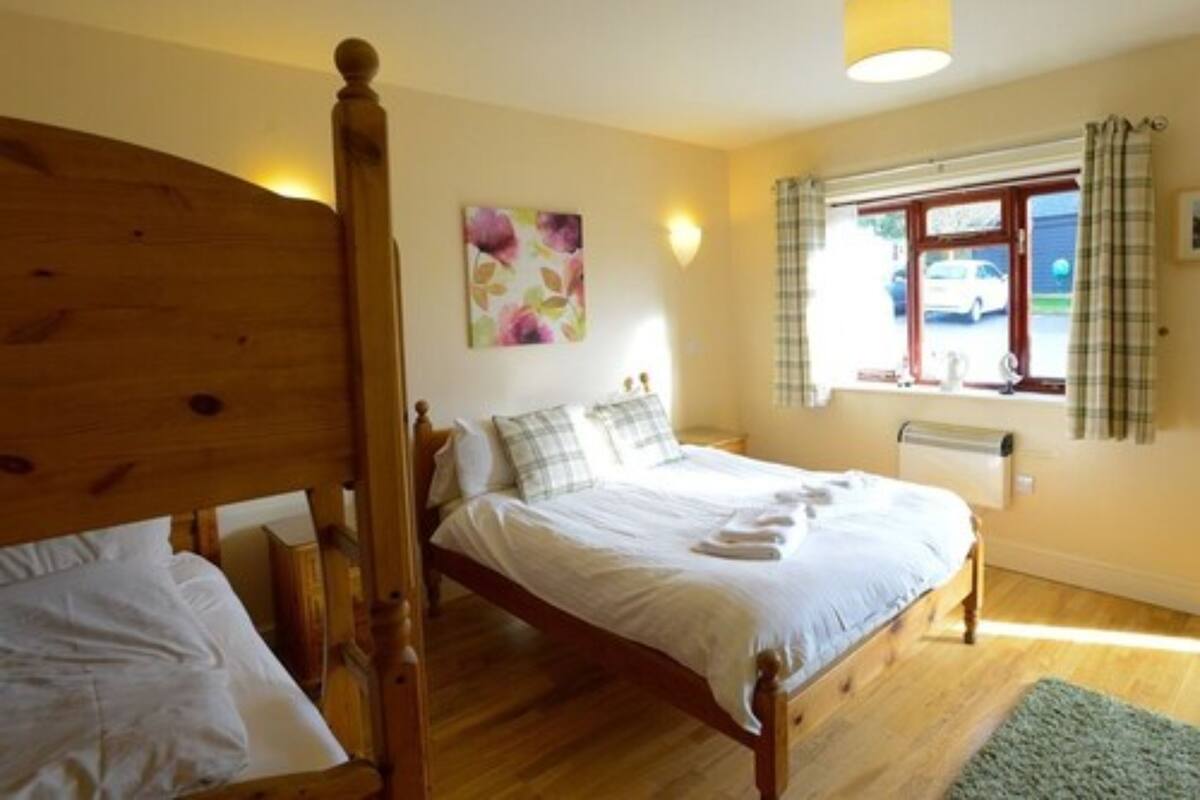 A bedroom with a wooden bed, a window with curtains, and a wall-mounted light fixture.
