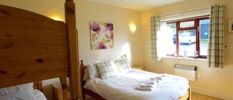A bedroom with a wooden bed, a window with curtains, and a wall-mounted light fixture.