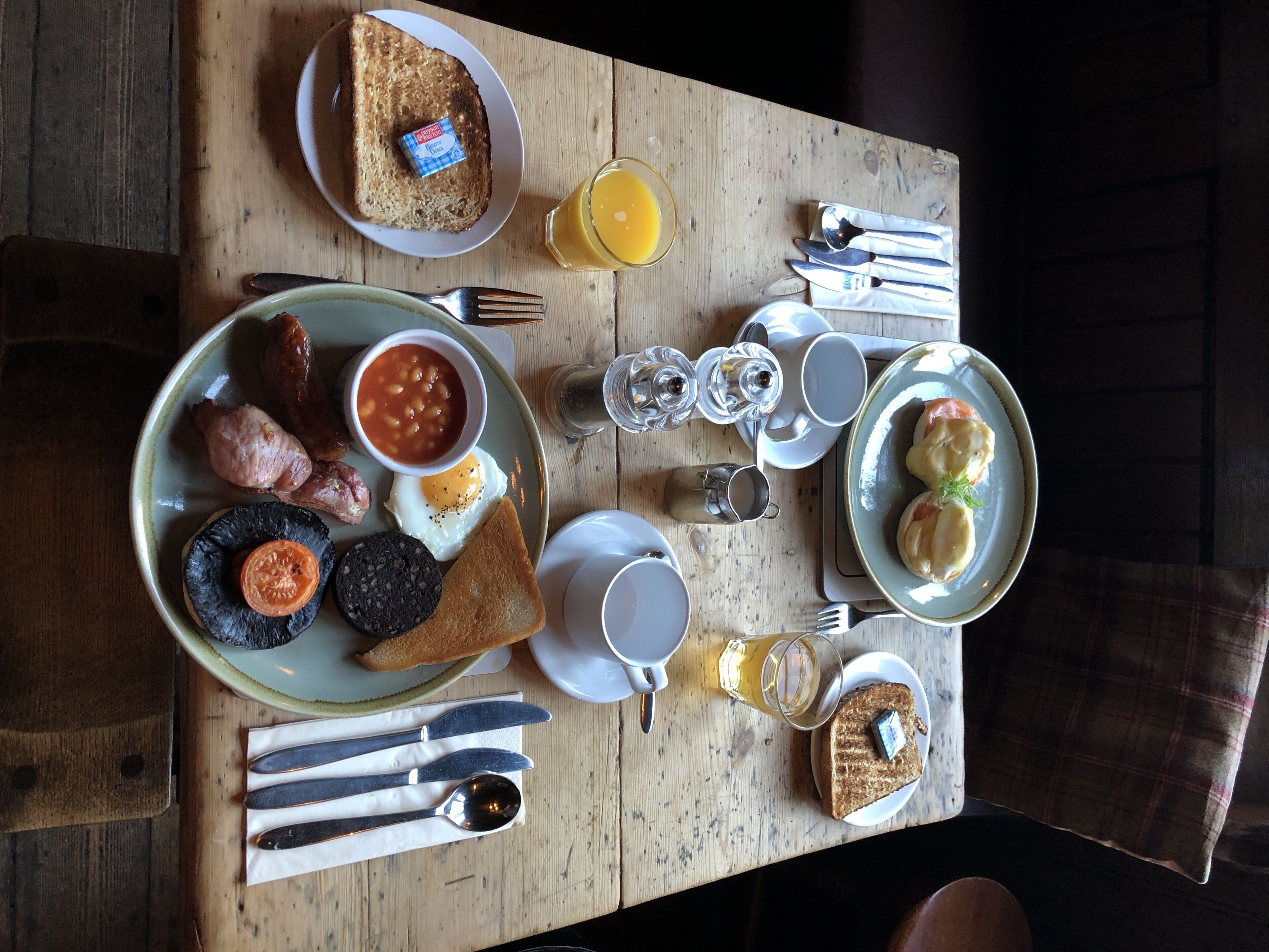 A breakfast table with toast, eggs, beans, sausages, and a variety of condiments.