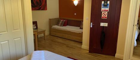 Habitación de hotel con cama, una mesita, un ventilador de pared, una puerta roja con un letrero y una pared roja con una pintura de rosa.