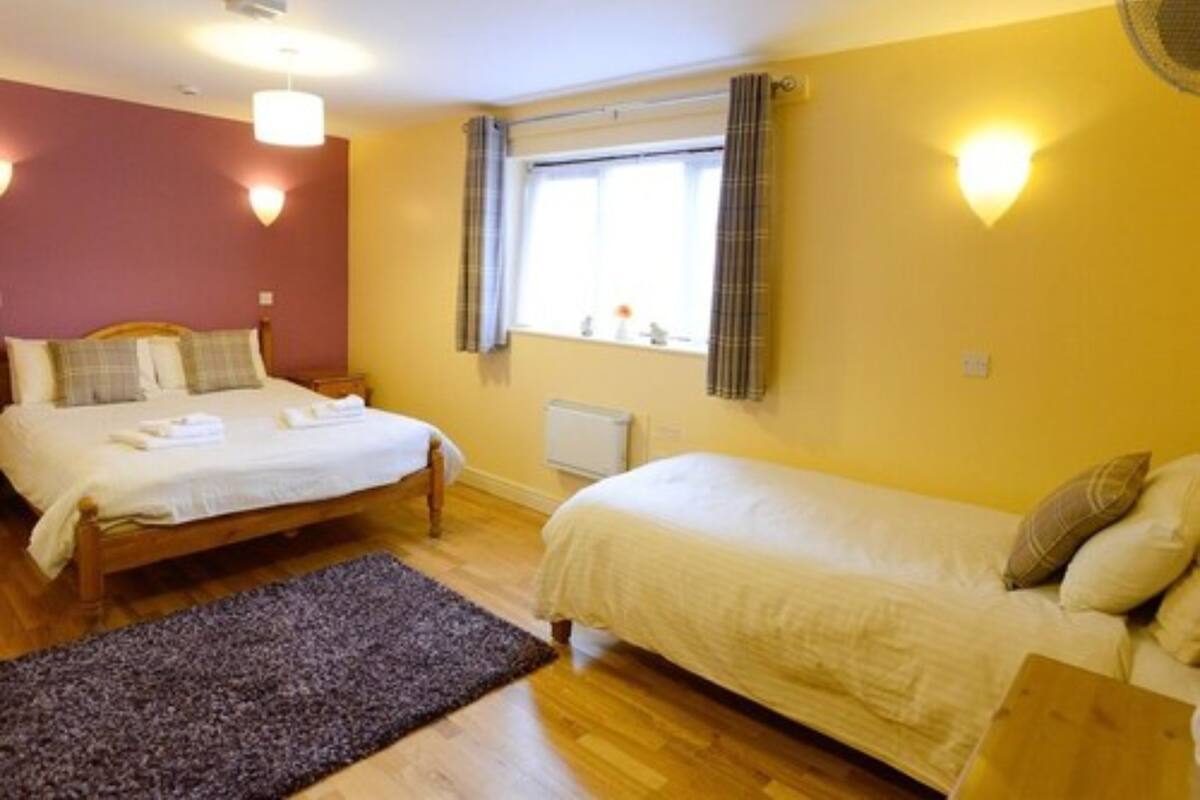 A hotel room with two beds, a window with curtains, a radiator, and a wooden floor.
