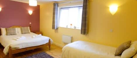 Une chambre d’hôtel avec deux lits, une fenêtre avec des rideaux, un radiateur et un plancher en bois.