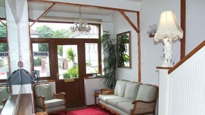 A room with a red carpet, wooden furniture, a chandelier, and a view through large windows. - The Braedene Lodge B&B (Paignton)