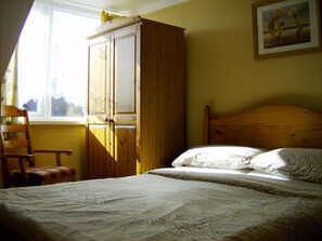 A bedroom with a wooden wardrobe, a bed with patterned bedding, a chair, and a painting on the wall. - The Braedene Lodge B&B (Paignton)