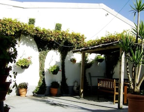 A white building with a covered patio area, potted plants, and a wooden bench. - The Braedene Lodge B&B (Paignton)