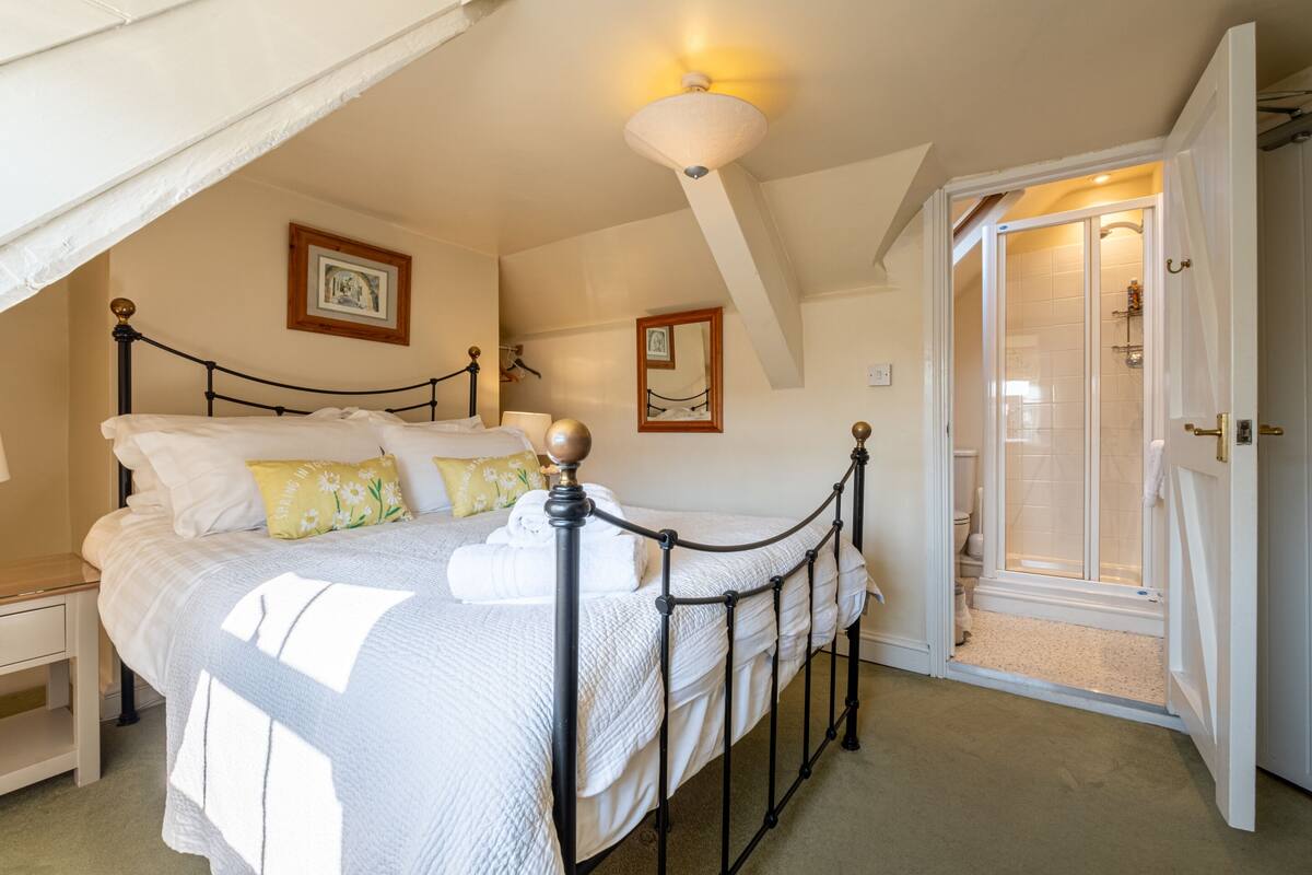 A bedroom with a bed, a nightstand, a bedside table, a ceiling fan, and a door leading to a bathroom.