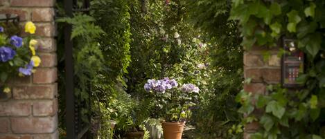 A brick archway leading to a garden with potted plants and flowers.