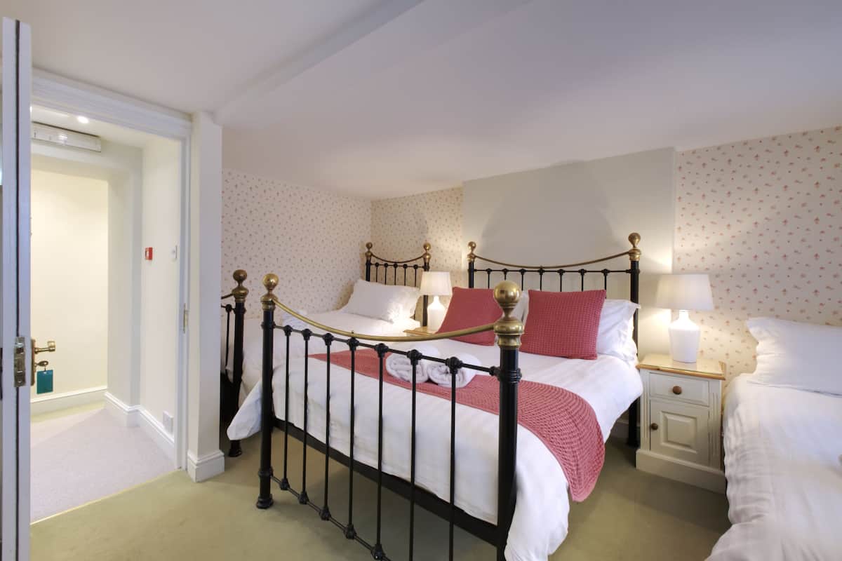 A bedroom with a four-poster bed, two bedside tables, and a door leading to another room.