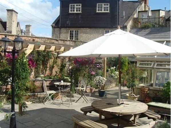 An outdoor patio with a round wooden table and chairs, surrounded by potted plants and a white umbrella. - The Old Brewhouse (Cirencester)