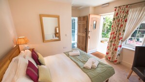 A bedroom with a bed, a mirror, a lamp, a door, and a window with curtains. - The Old Brewhouse (Cirencester)
