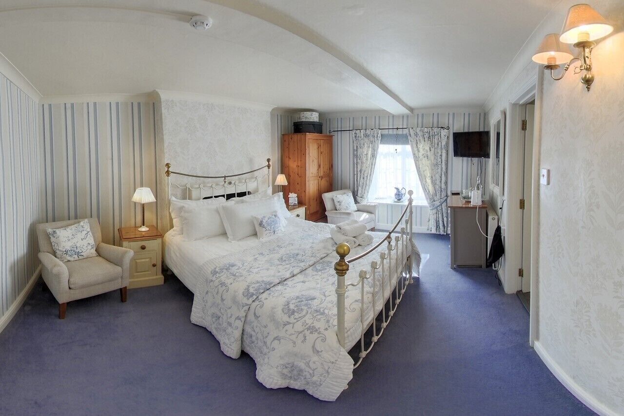 A bedroom with a large bed, a nightstand, a chair, a wardrobe, a desk, and a television.