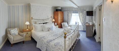 A bedroom with a large bed, a nightstand, a chair, a wardrobe, a desk, and a television.