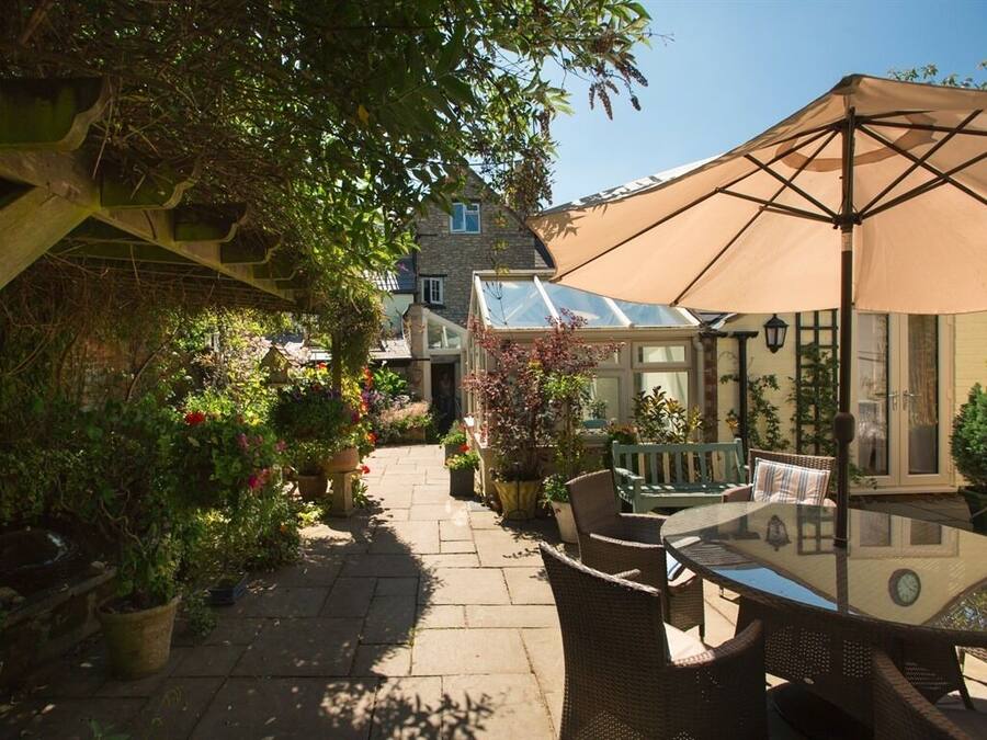A patio area with a glass table and wicker chairs, surrounded by potted plants and a large umbrella.