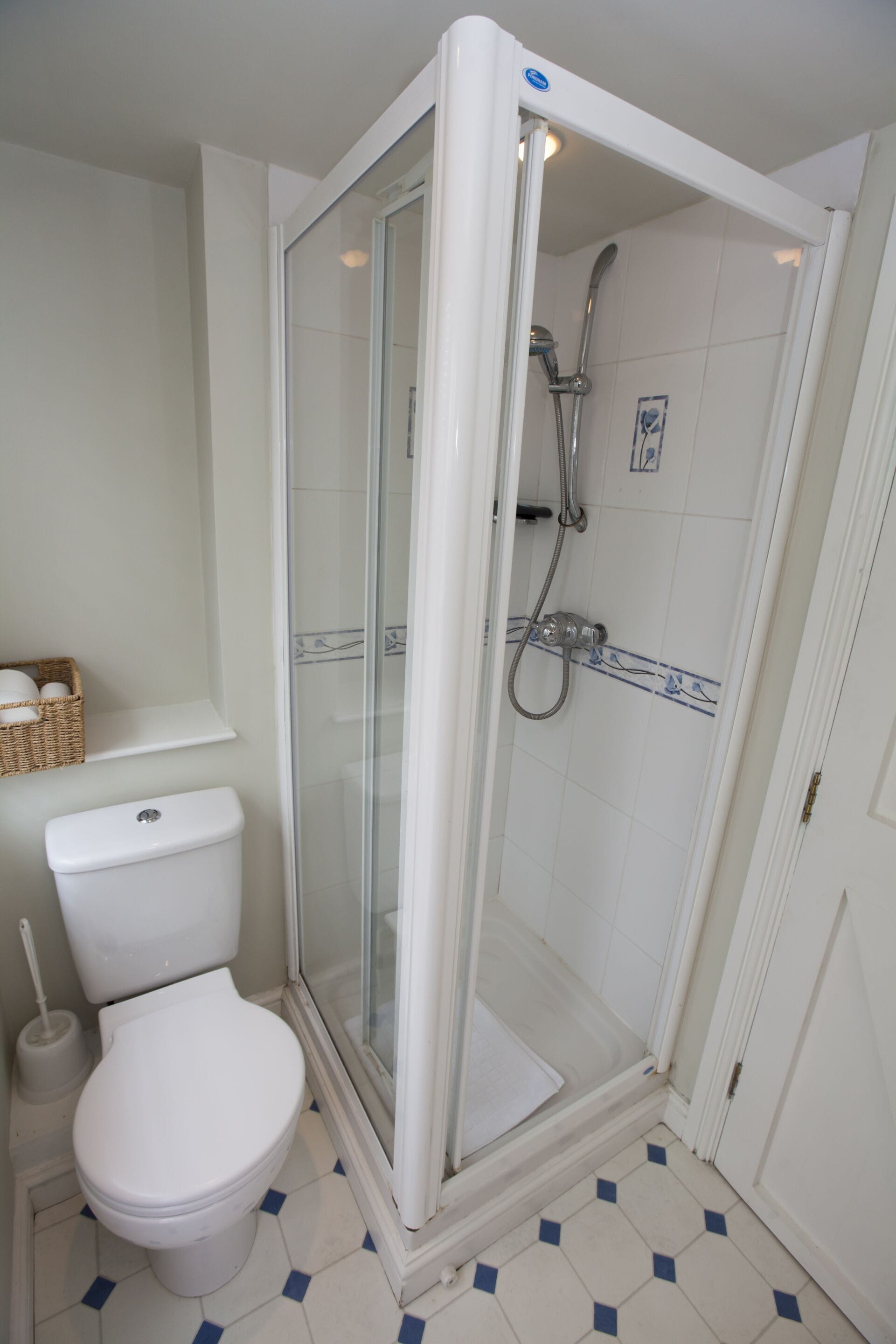 A bathroom with a toilet, a shower enclosure, and a tiled floor.
