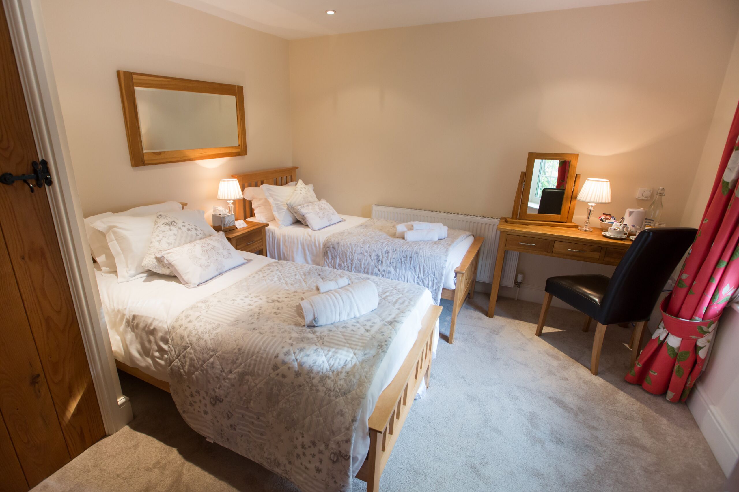 A hotel room with two beds, a desk, a chair, and a mirror.