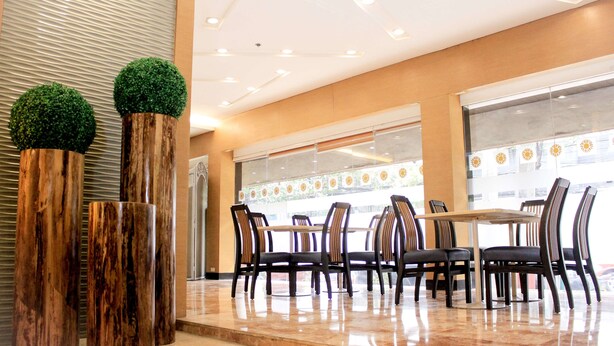 A modern dining area with a polished marble floor, wooden columns with green topiary, and a large window with a view of the street. - Palm Hotel Manila (Manila)